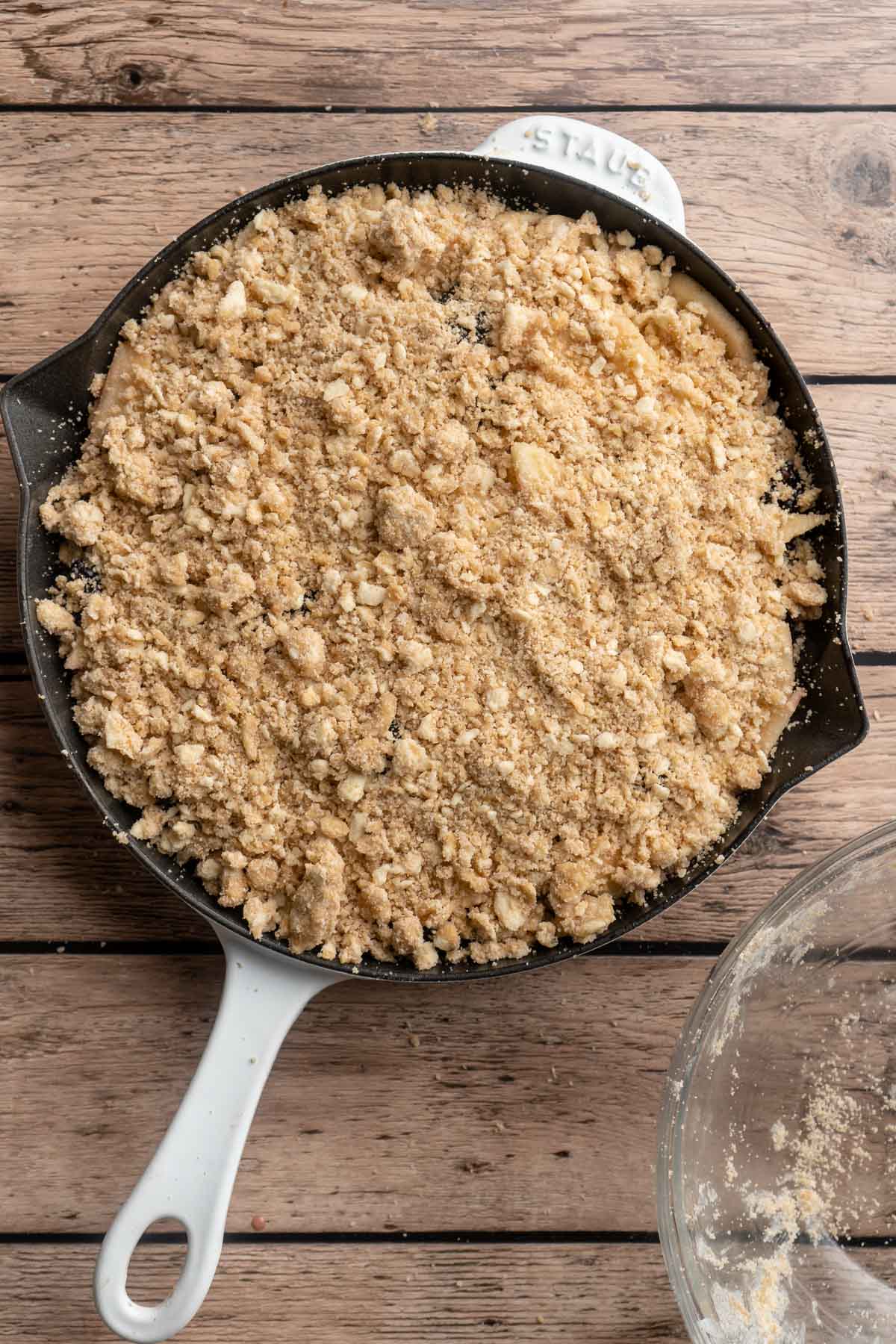 Adding crumble topping over fruit filling in a cast iron skillet.