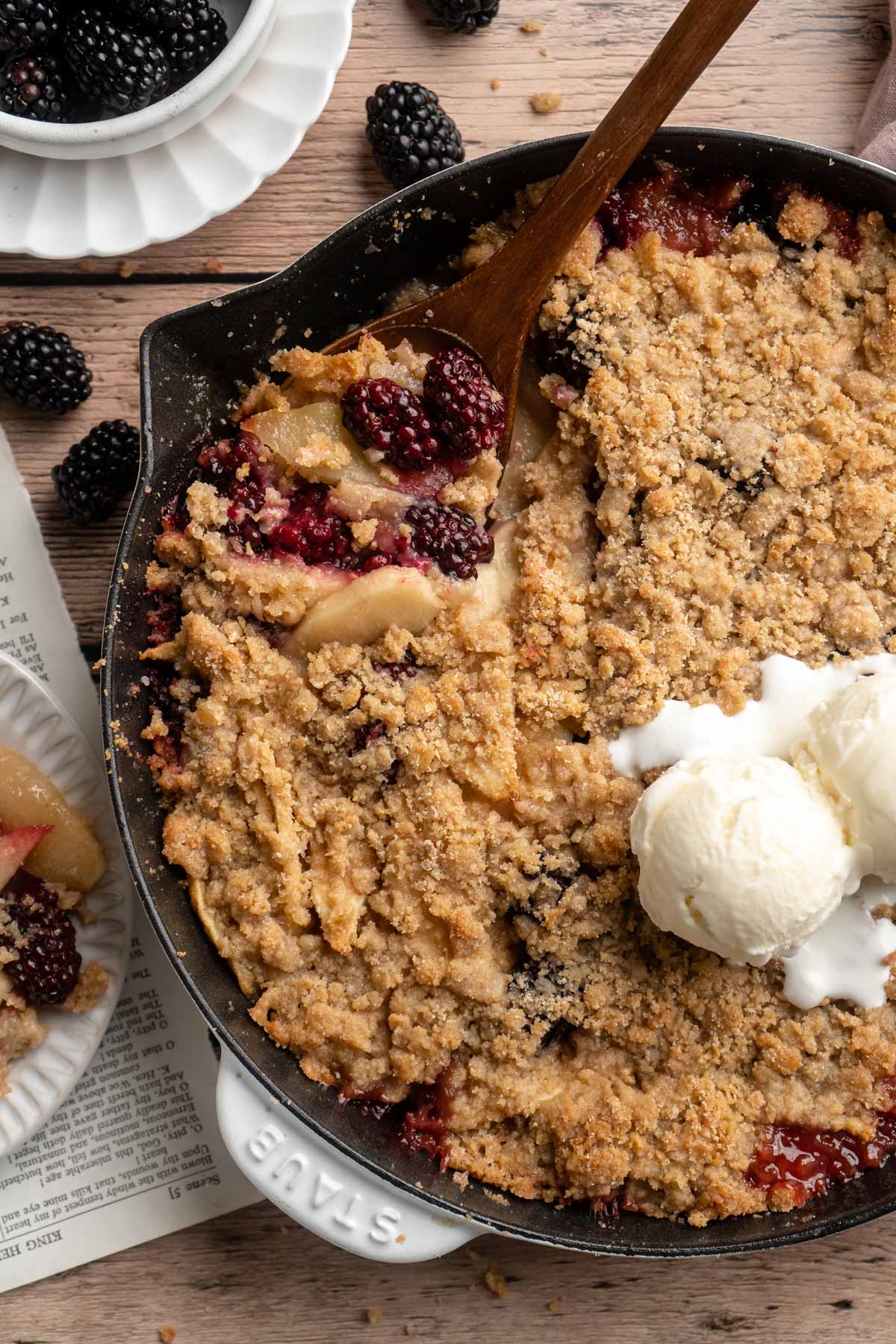 Apple blackberry crumble in a cast iron skillet topped with a scoop of vanilla ice cream.