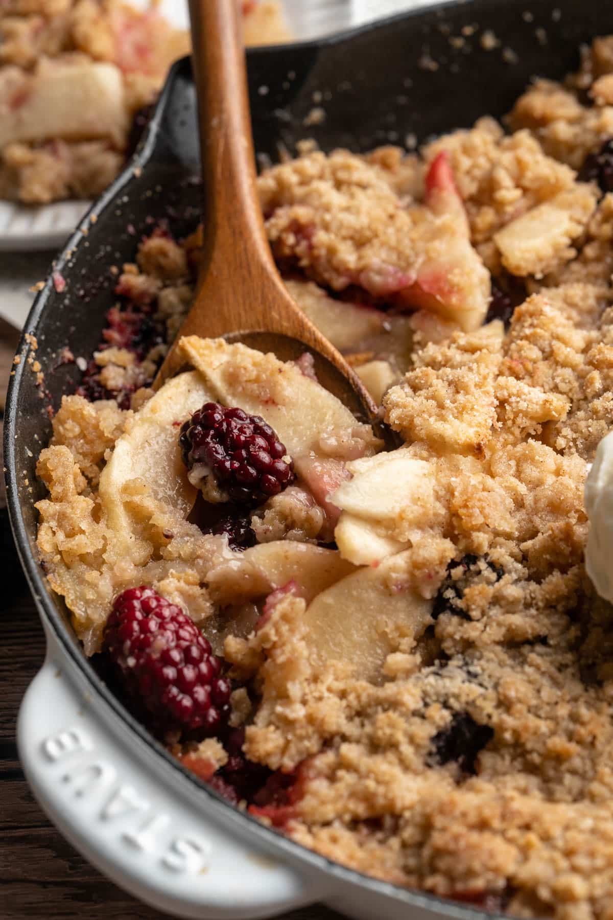 Wooden spoon serving apple blackberry crisp.