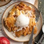 Serving of apple dump cake topped with a scoop of ice cream on a plate.