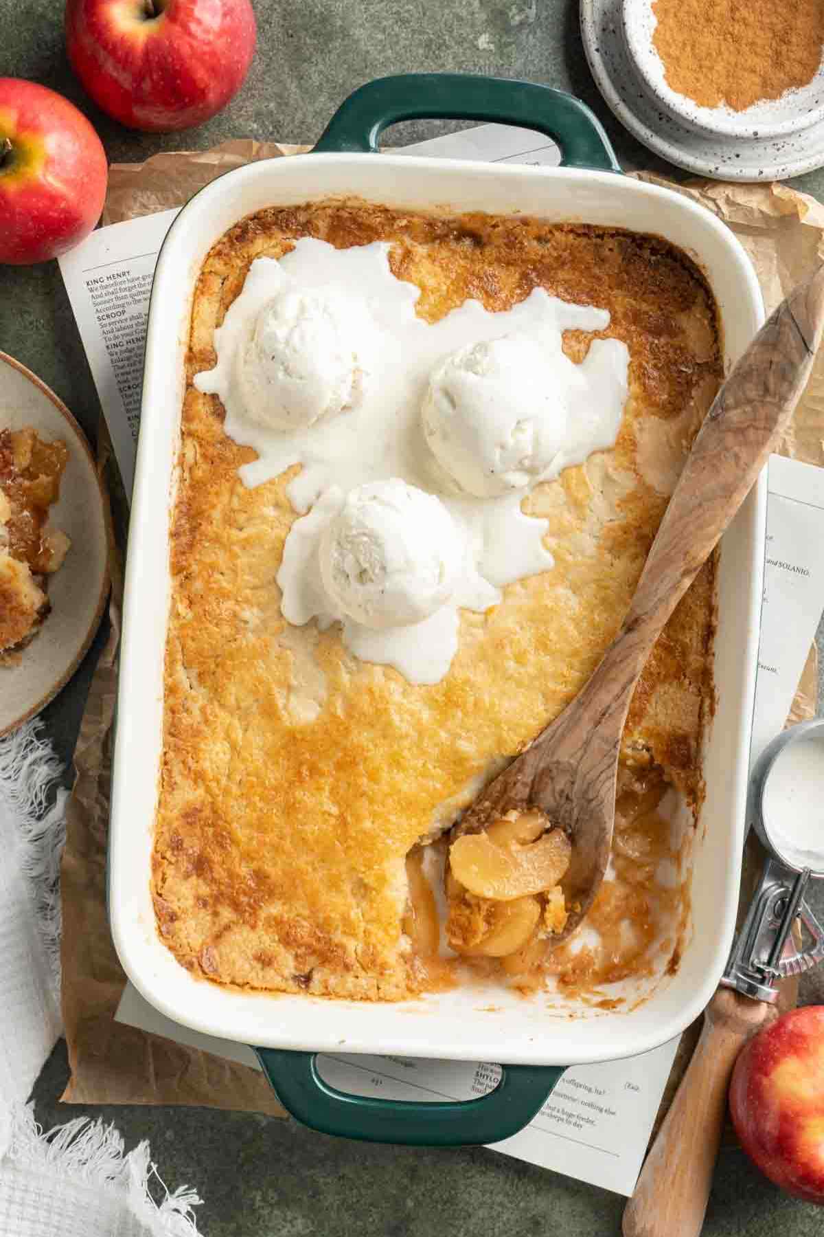 Serving an apple dump cake that is topped with scoops of ice cream with a wooden spoon.