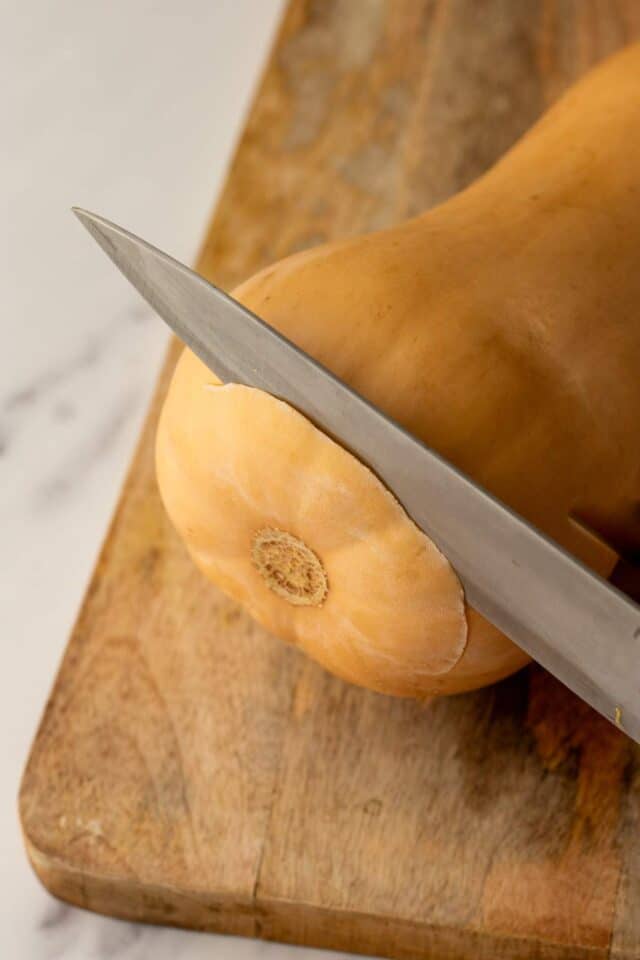 Using a knife to cut off the bottom of a butternut squash.