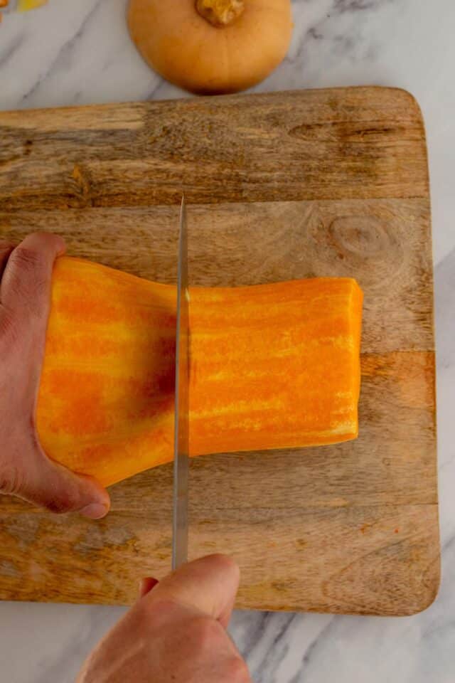 Using a knife to cut a squash in half on a cutting board.