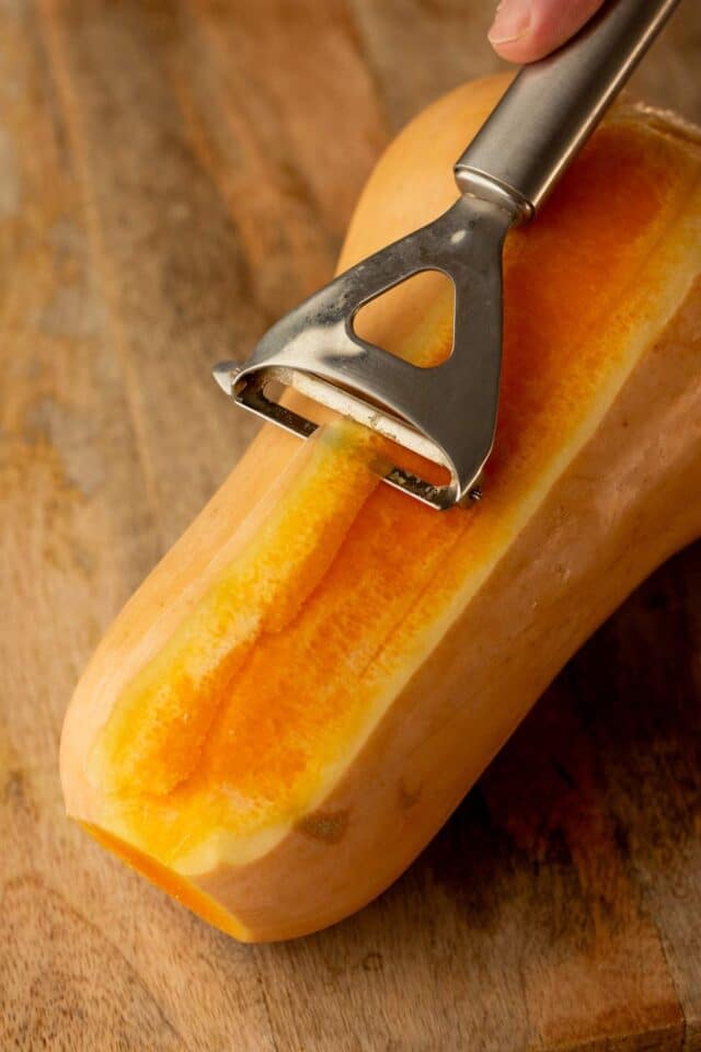 Using a vegetable peeler to peel a butternut squash 