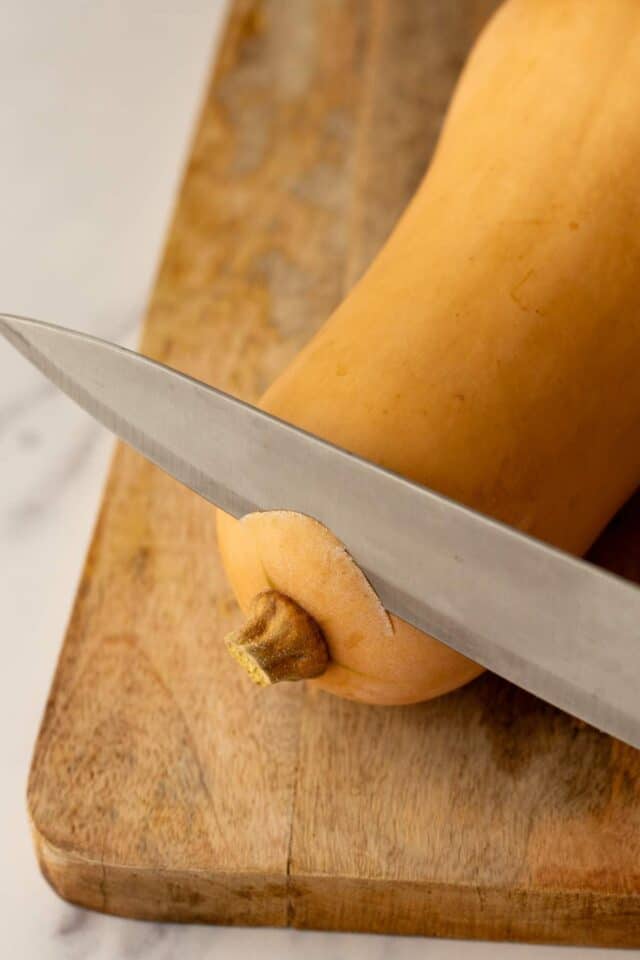 Using a knife to slice off the top of a butternut squash.