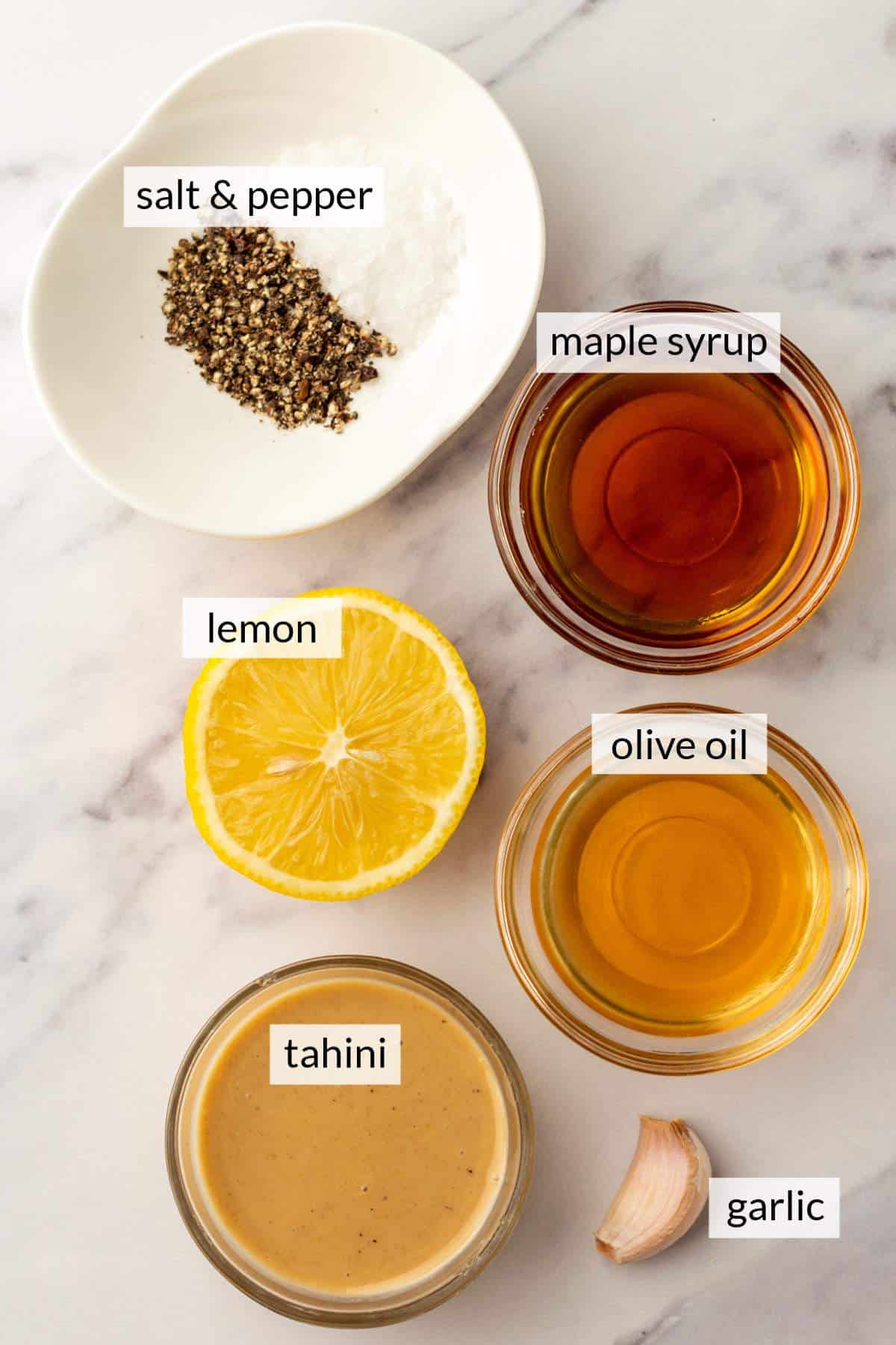 Bowls of tahini, olive oil, and maple syrup near a sliced lemon.