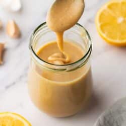 Using a spoon to mix a small jar of tahini dressing.