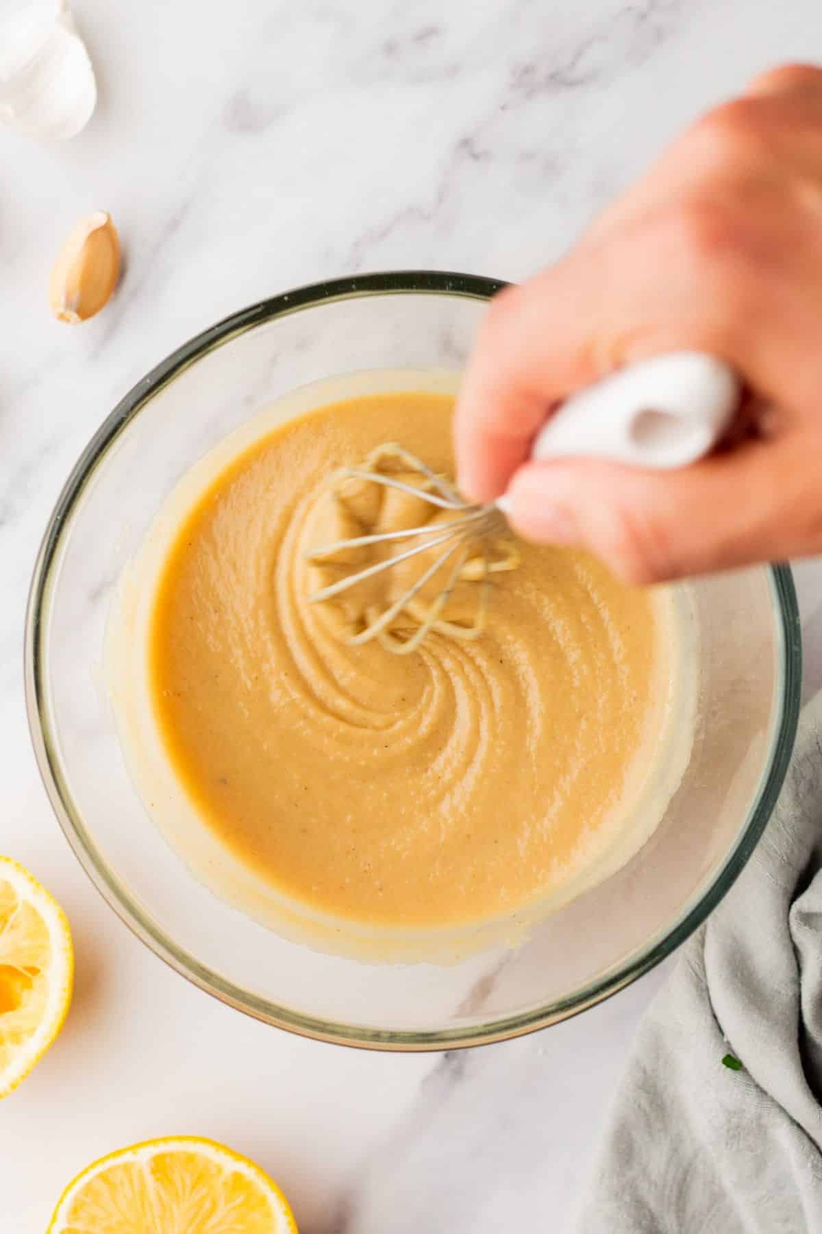 Whisking tahini dressing in a small bowl.