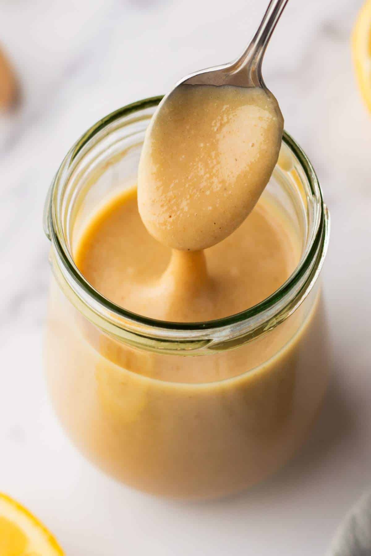 Maple tahini dressing in a small glass jar with a spoon. 