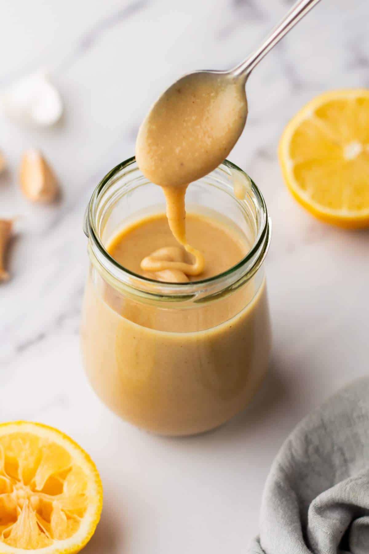 Using a spoon to mix a small jar of tahini dressing.