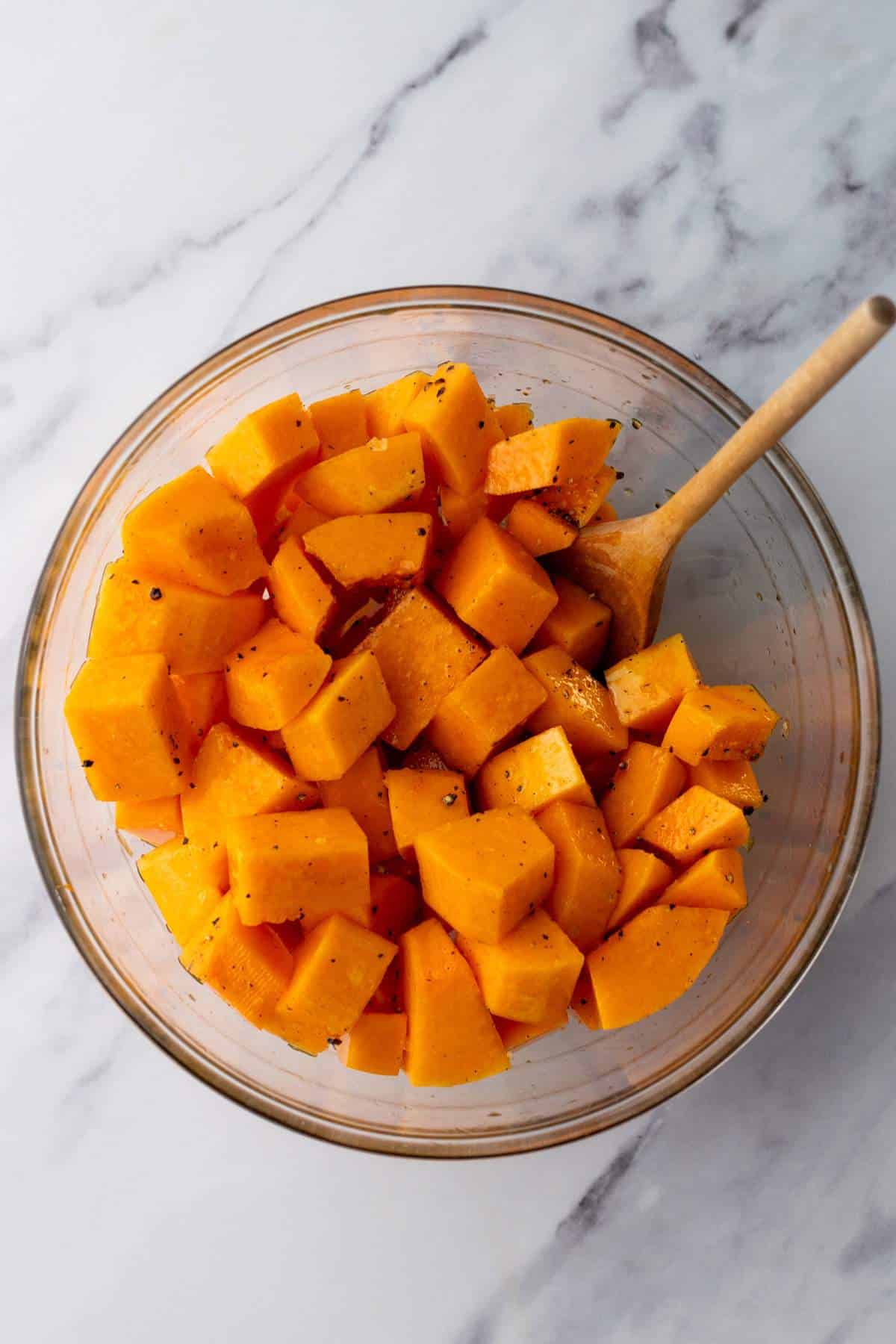 Tossing butternut squash with oil and seasonings in a bowl.