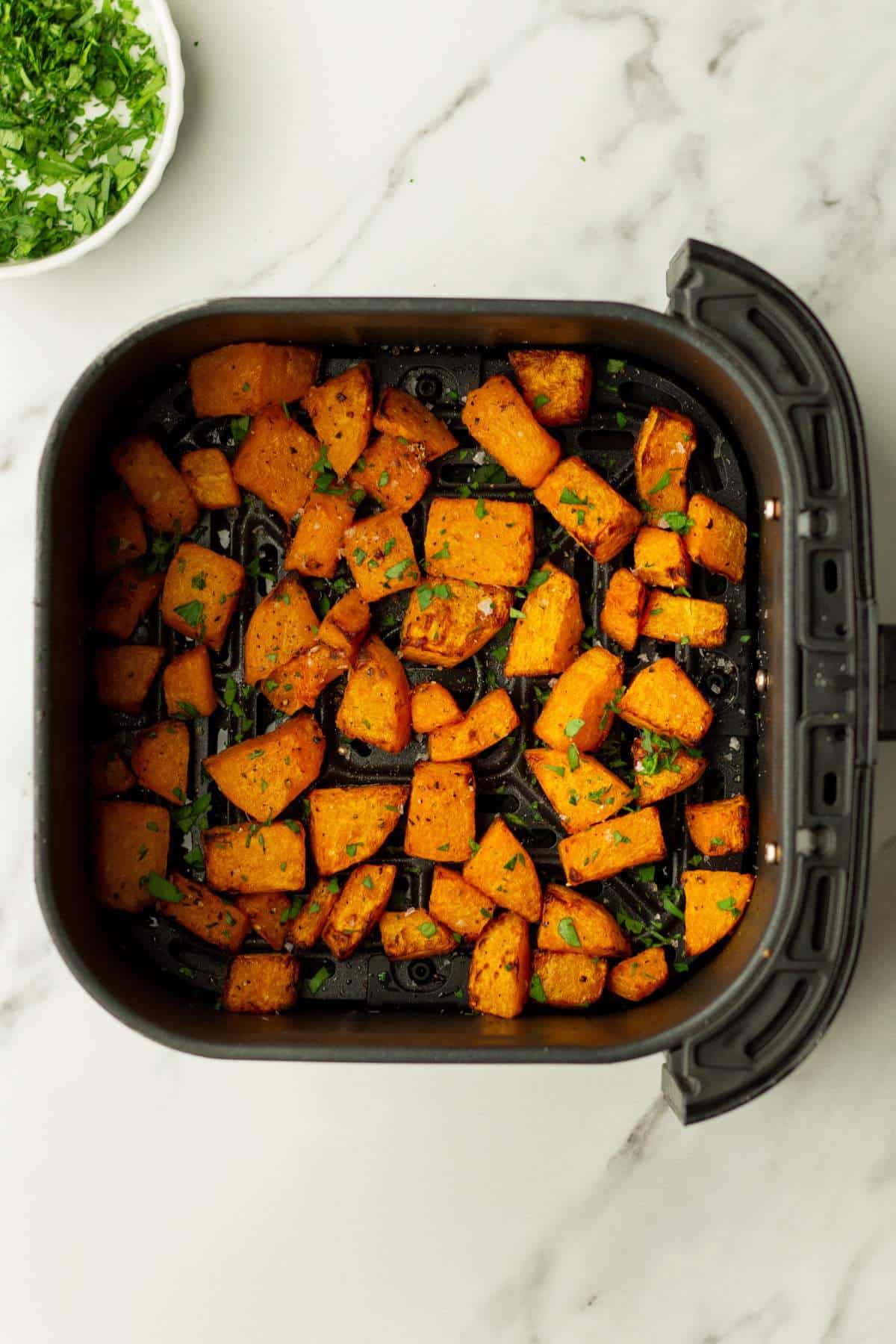 Air fryer butternut squash garnished with herbs.