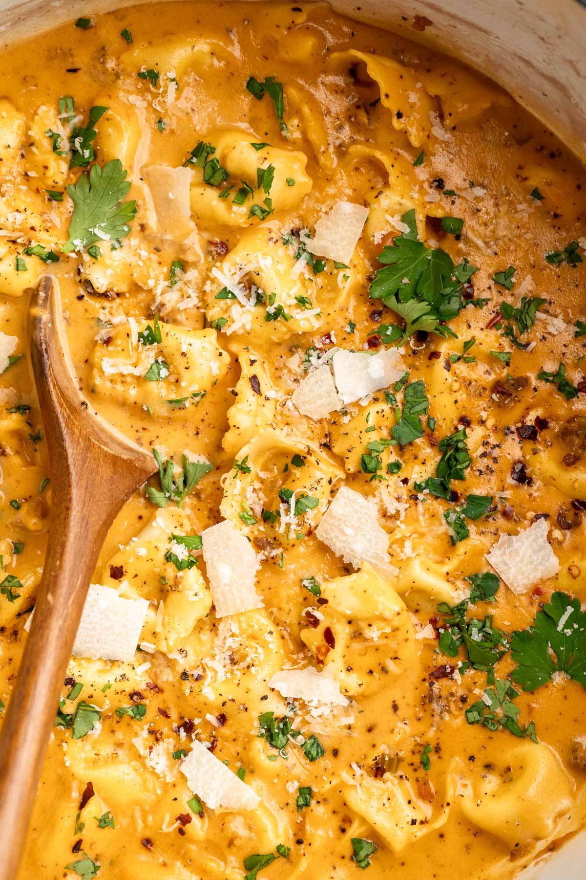 Using a wooden spoon to stir creamy tortellini soup garnished with parsley and parmesan cheese.