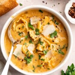 Creamy tortellini soup in a bowl garnished with fresh parmesan and parsley.