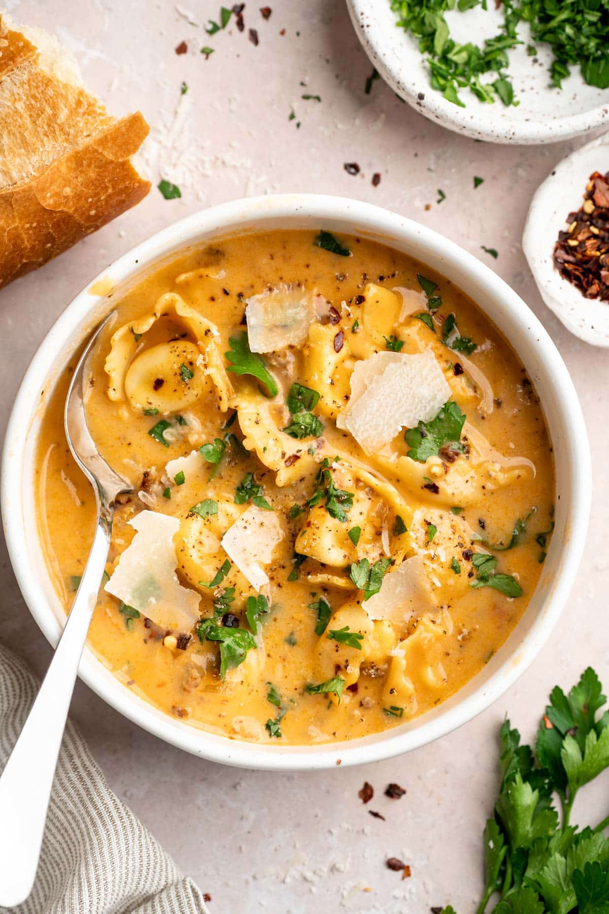 Creamy tortellini soup in a bowl garnished with fresh parmesan and parsley.