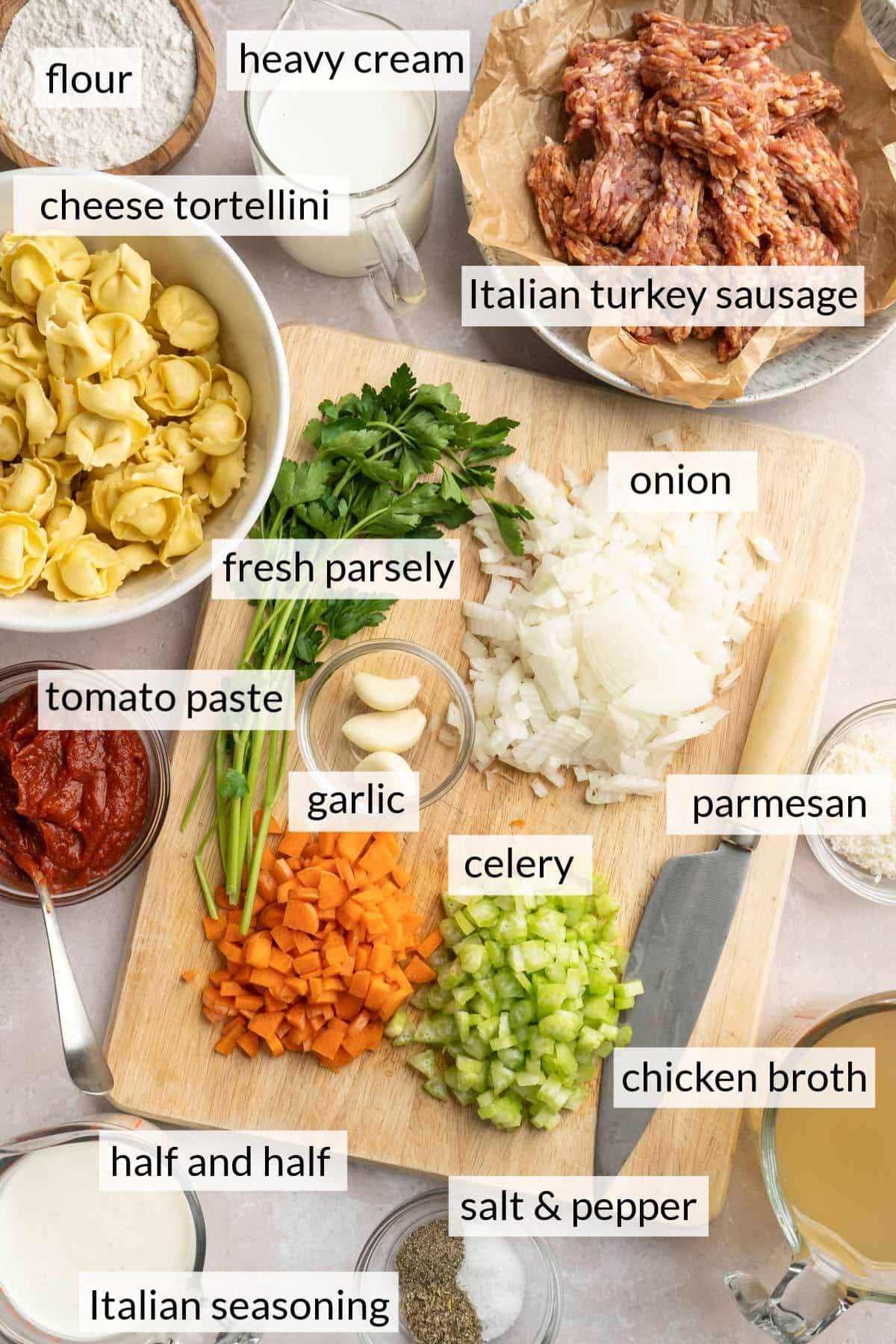 A bowl with tortellini near a cutting board with diced carrot, celery and onion.