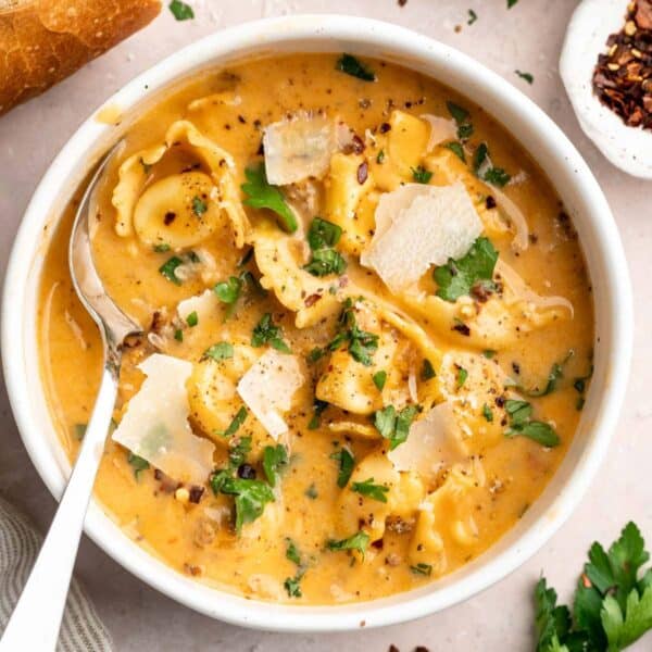 Creamy tortellini soup in a bowl garnished with fresh parmesan and parsley.