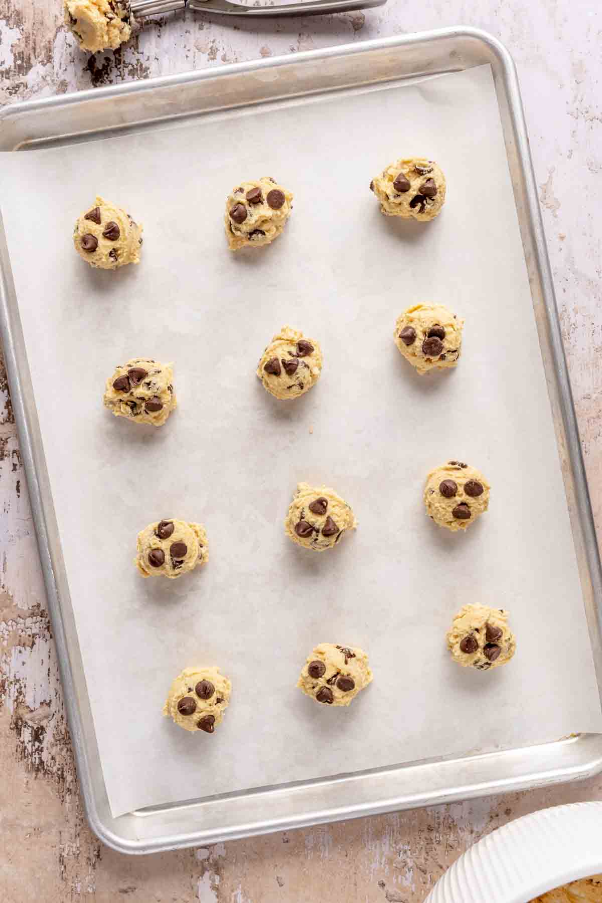 Cookie dough balls on a parchment lined baking sheet.