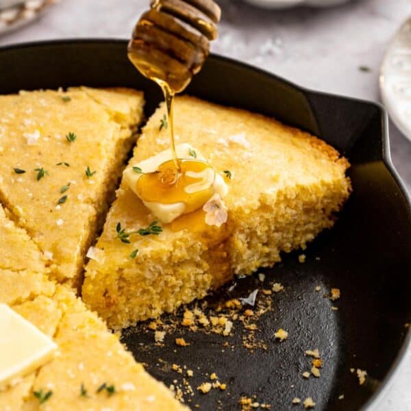 Sliced skillet cornbread with a pat of butter being drizzled with honey.