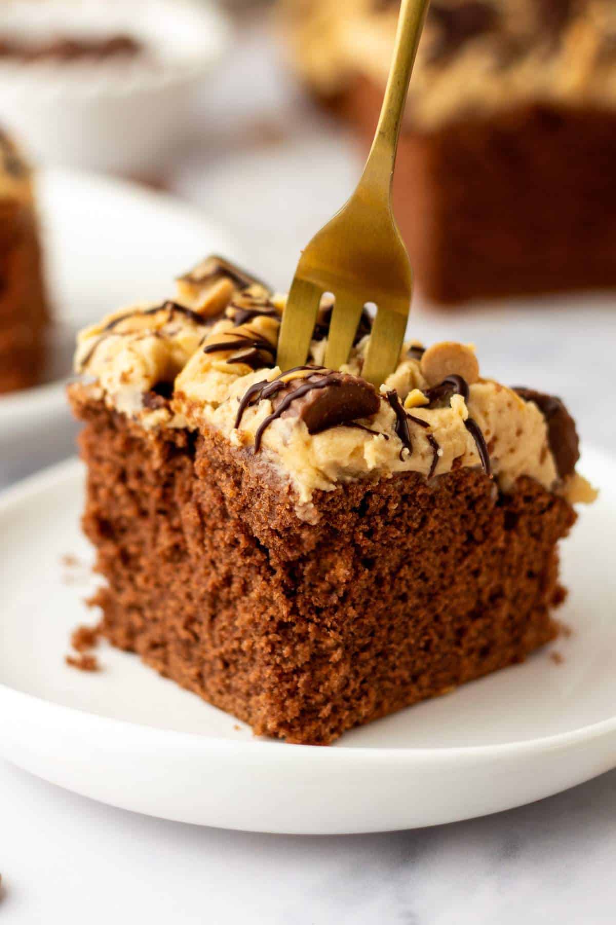 Slice of chocolate cake with peanut butter frosting on white plate with a fork.